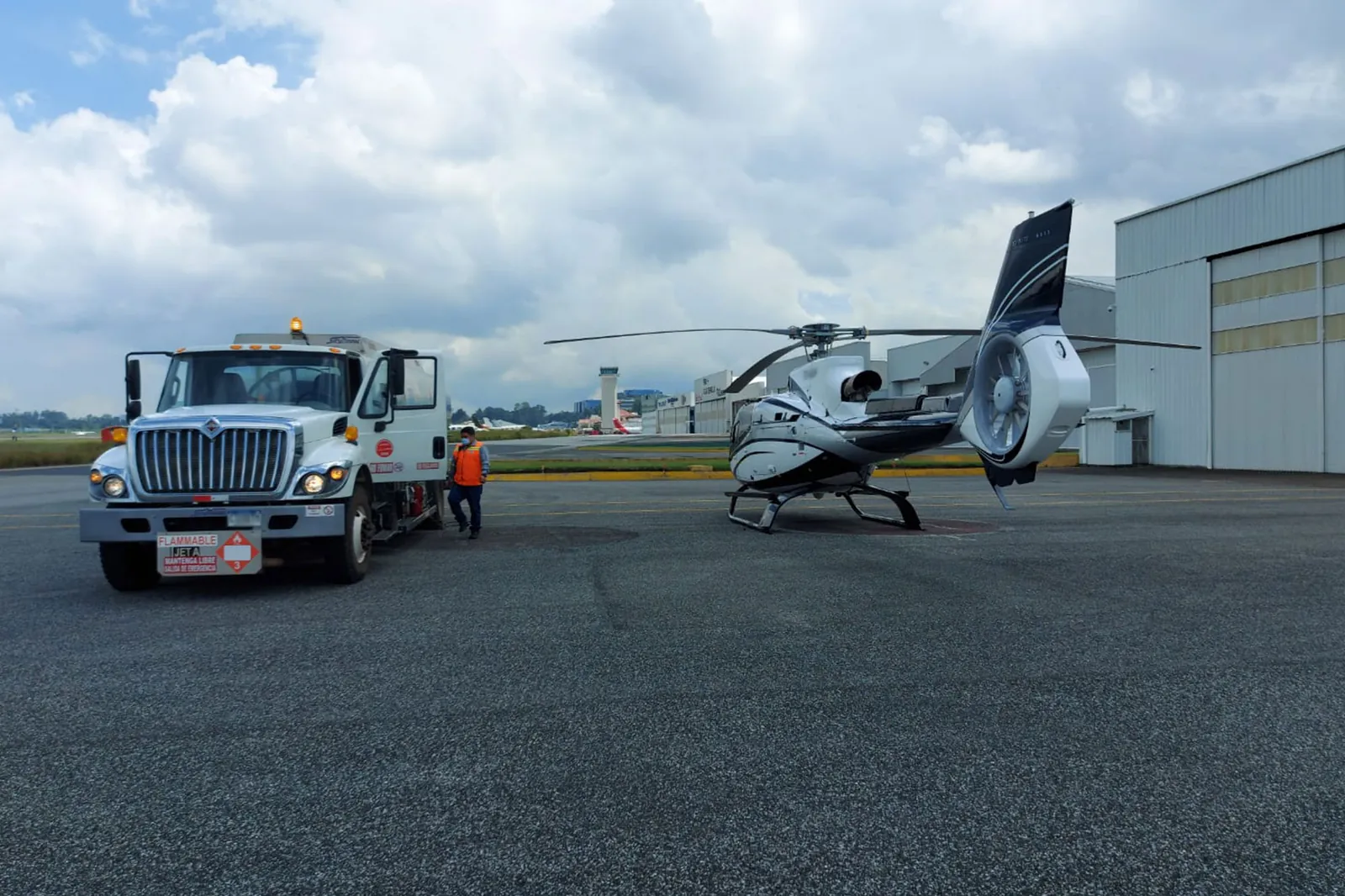 Camión de combustible estacionado junto a un helicóptero en la plataforma de un aeródromo
