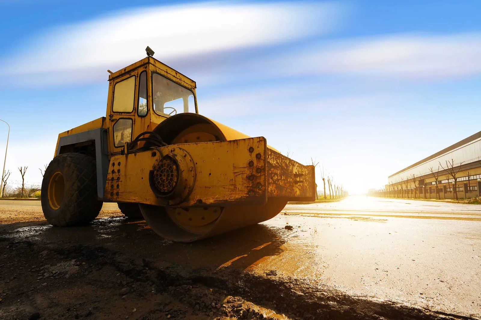 Rodillo compactador amarillo sobre una vía en construcción, a contraluz