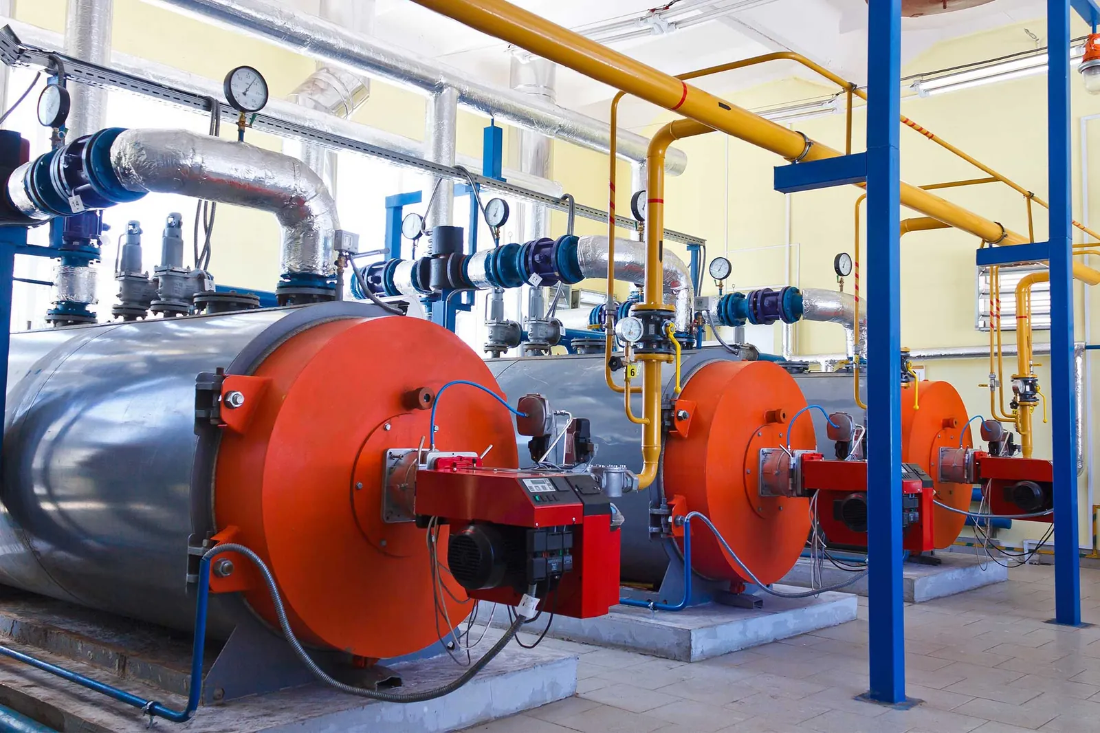 Calderas industriales con quemadores rojos y tuberías en una sala de máquinas